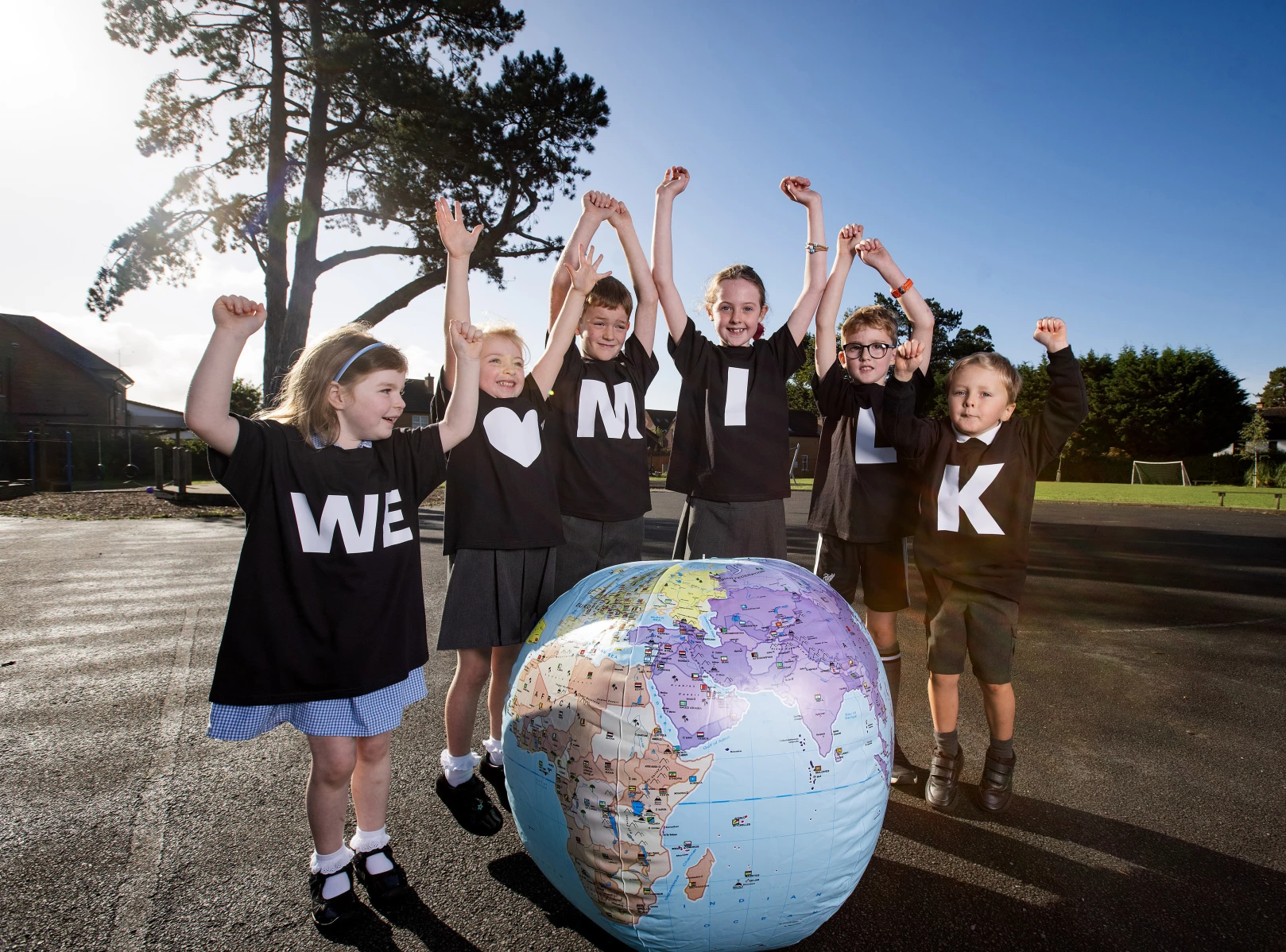 Lie-up of six primary school children gathered around an inflatable globe wearing black t-shirts that spell out: 'We love milk'